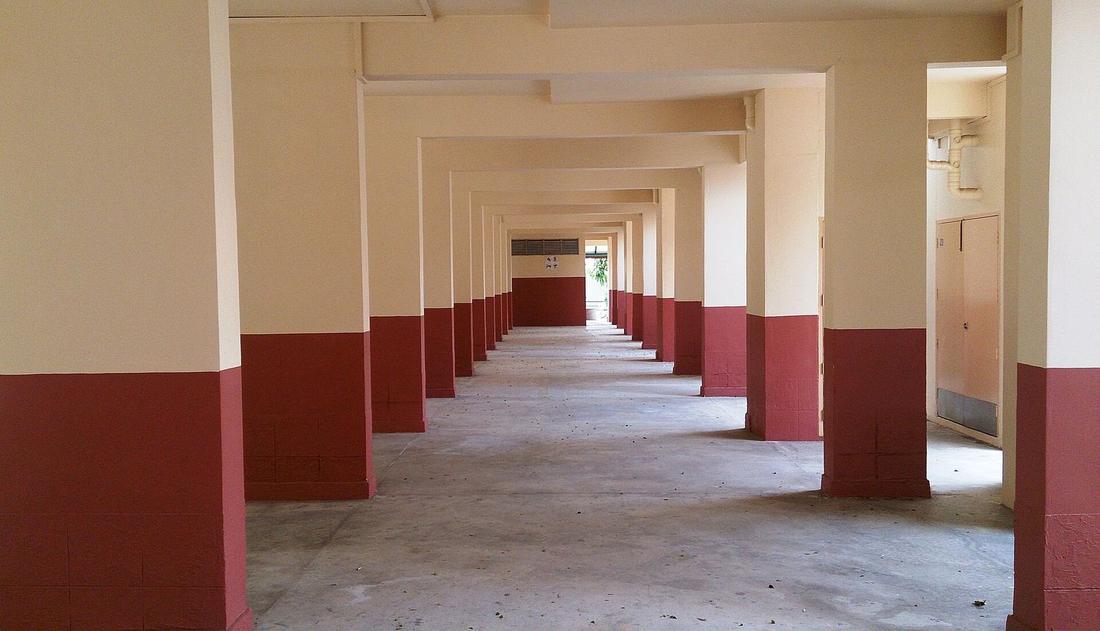 A long HDB corridor of cream pillars with red bases.